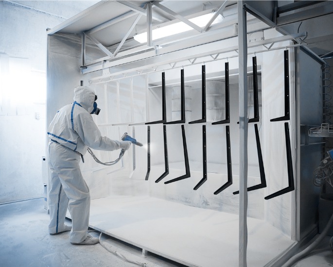 A professional applying powder coating to new parts, part of the services offered by DMi